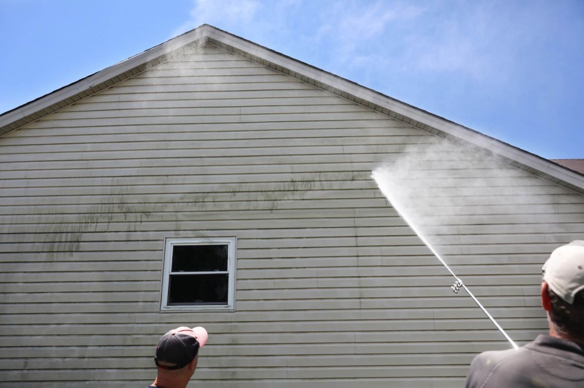 A person pressure washing a light colored house.